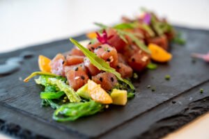 Ceviche de corvina con dados de pescado marinado, wakame, cítricos y brotes frescos servido sobre pizarra negra.